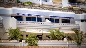 A hotel with a white facade, blue awnings, and a balcony with plants. - Palm Suites (Mogan)