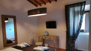 A hotel room with a bed, a desk, a chair, a mirror, a television, and a window with curtains. - Farmhouse 2: authentic Tuscan house (Dicomano)