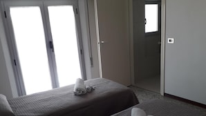 Ein Hotelzimmer mit zwei Betten, einer Schiebetür und einem kleinen Fenster.