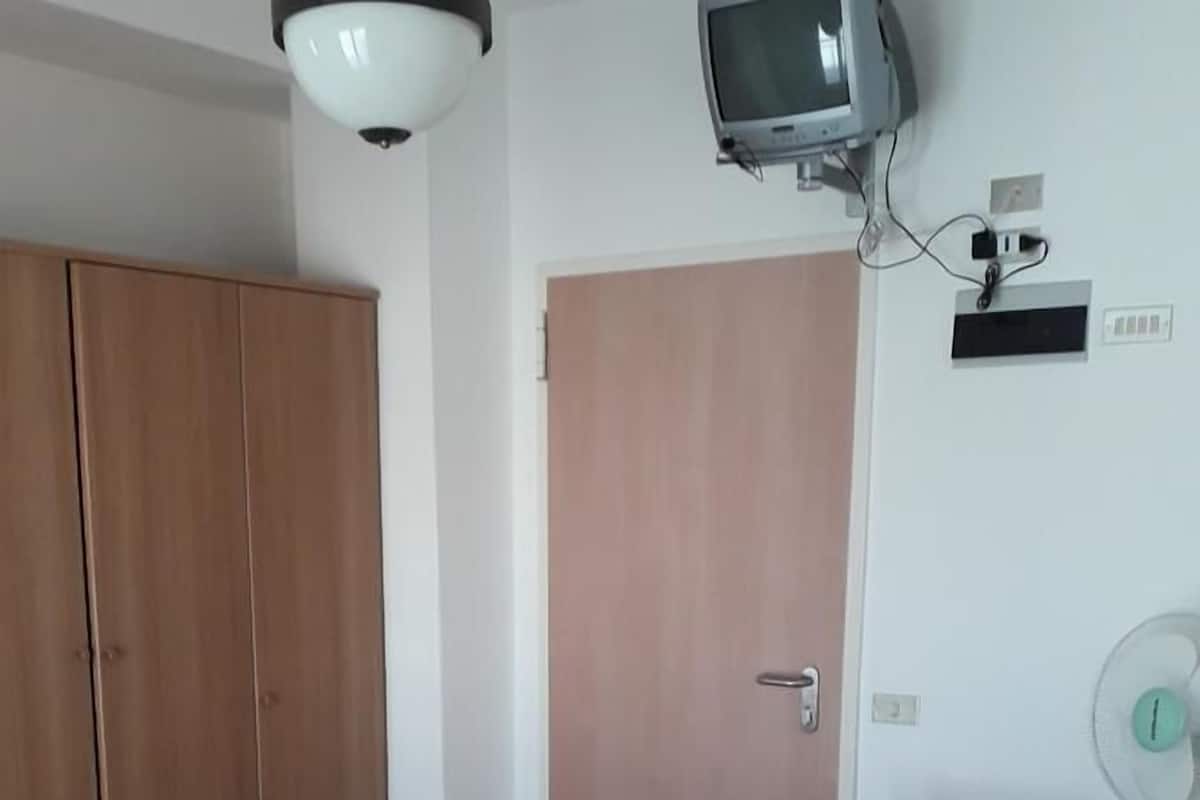 Een hotelkamer met twee bedden, een garderobe, een televisie en een bureau met een ventilator.