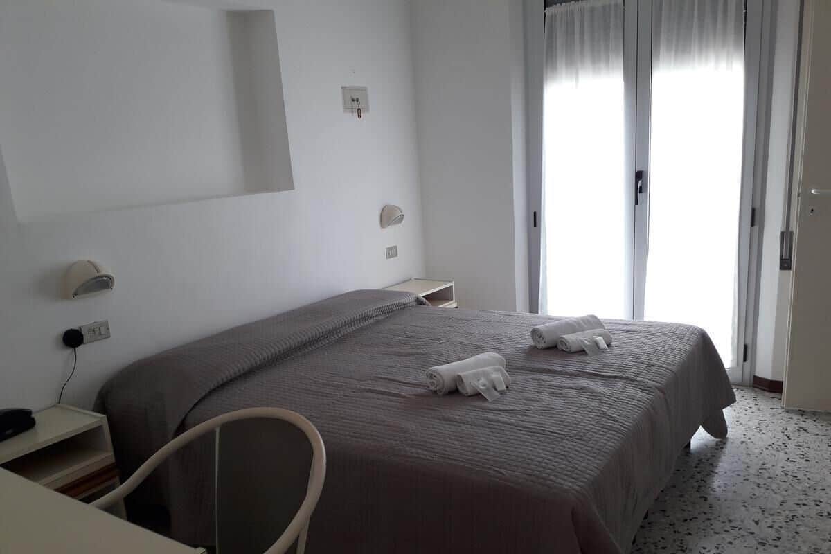Een hotelkamer met een bed, een bureau, een stoel en een raam met gordijnen.