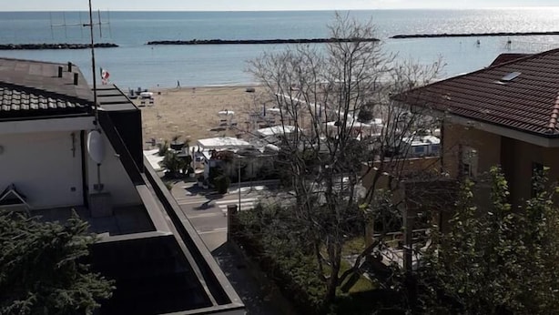 Ein Wohngebiet mit Blick auf den Strand und das Meer. Es sind Häuser mit Ziegeldächern und eine Straße im Vordergrund zu sehen.