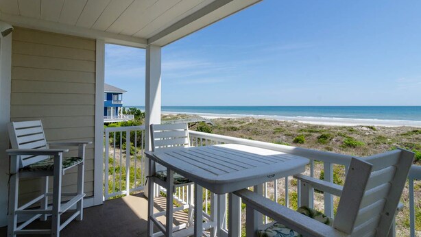 A covered outdoor area with a table and chairs, overlooking a beach.