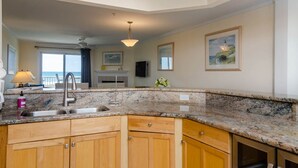 A kitchen with granite countertops, wooden cabinets, a double sink, and a view of the ocean.