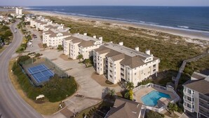 A coastal hotel with multiple buildings, a swimming pool, and a tennis court.