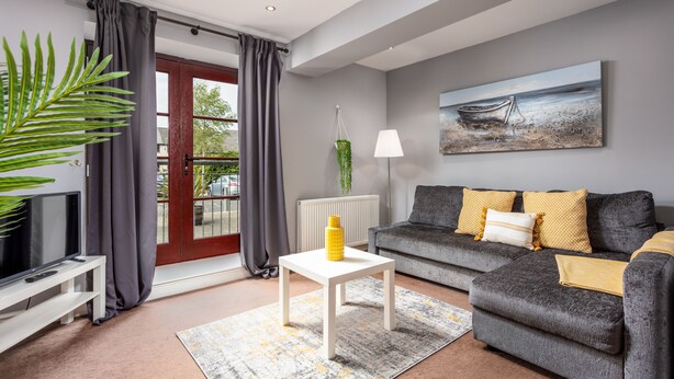 A modern living room with a grey sofa, a white coffee table, and a painting of a boat on the wall. - Elliot Suite No3 - Donnini Apartments (Ayr)