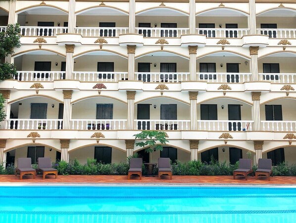Un hotel con varios balcones, piscina y mobiliario de exterior.