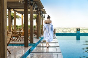 Un espace aménagé au bord de la piscine, avec des pergolas en bois, des sièges d’extérieur et une vue sur le paysage urbain.