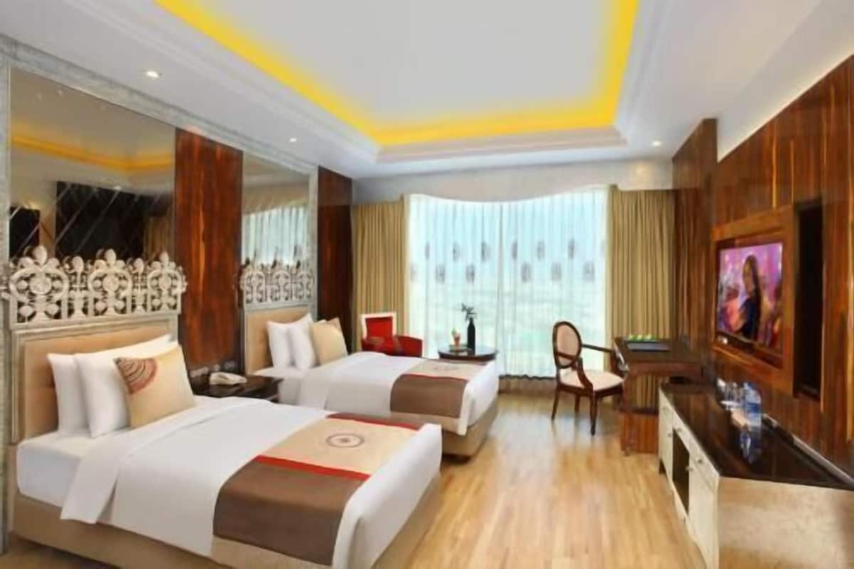 A hotel room with two beds, a TV, a desk, and a large window.