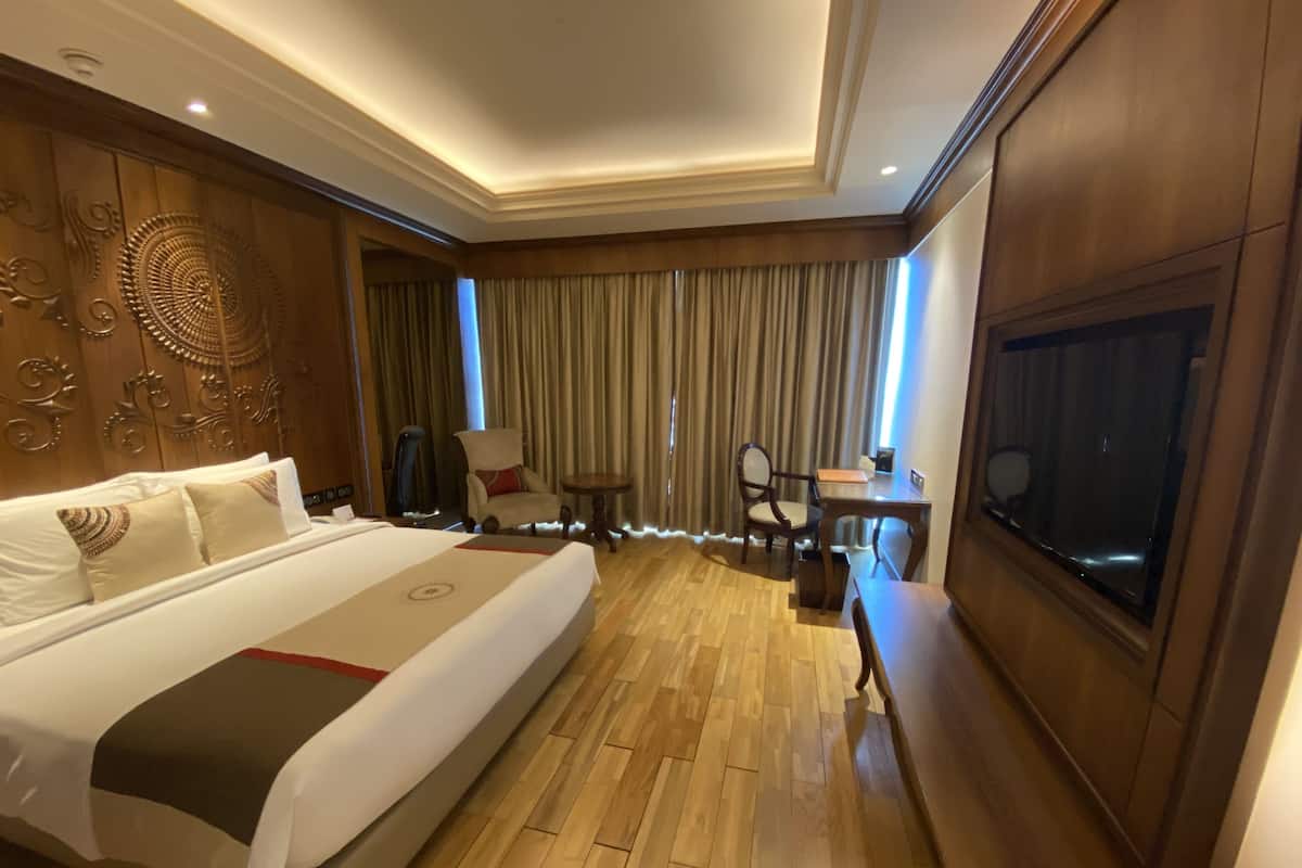 A hotel room with a large bed, a desk, a chair, a TV, and a window with curtains.
