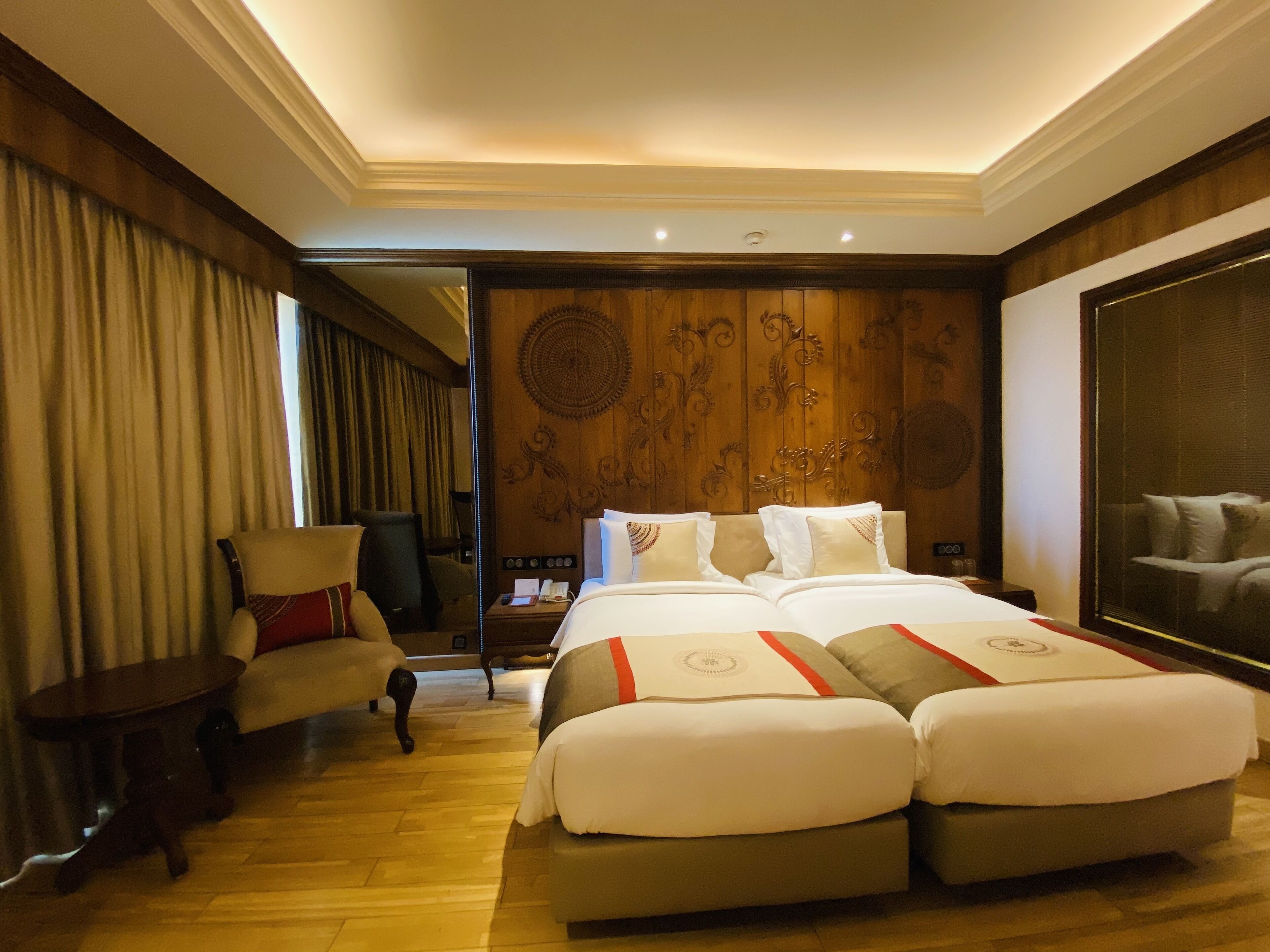 A hotel room with a large bed, a chair, a small table, and a large mirror.