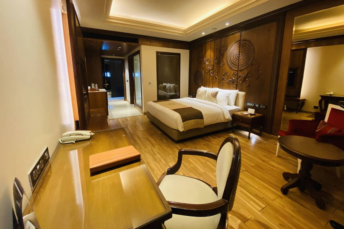 A hotel room with a large bed, a desk, a chair, a table, and a mirror.