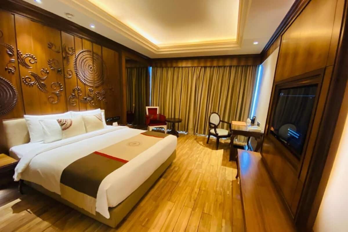 A hotel room with a large bed, a desk, a chair, a TV, and a curtain.