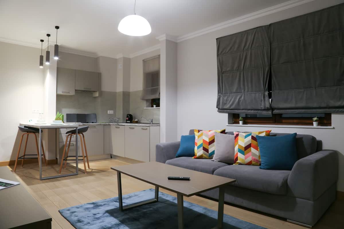 Una sala moderna con un sofá gris, una mesa de centro y un comedor con una cocina al fondo.