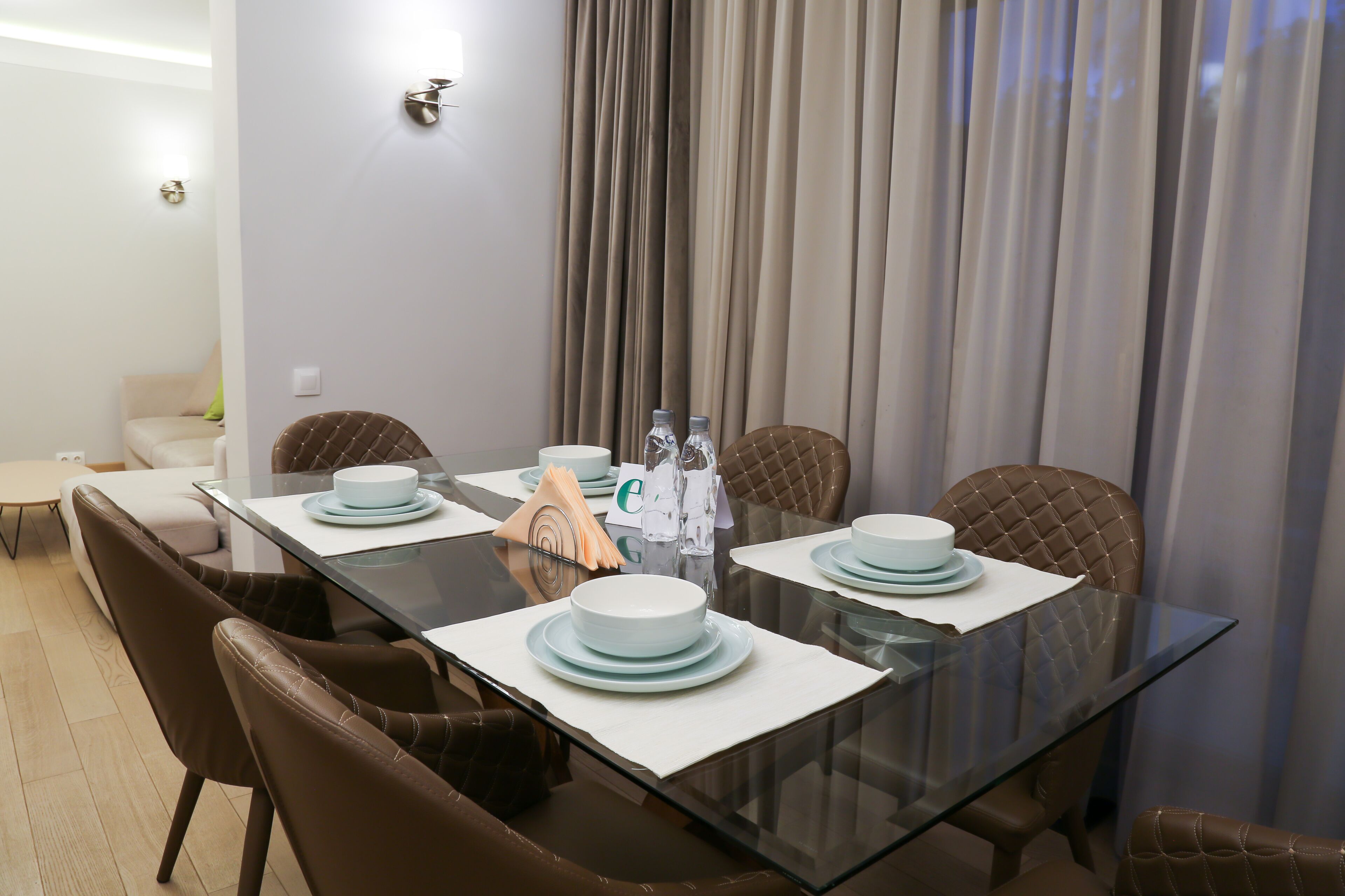 A dining area with a glass table, brown upholstered chairs, and white plates.