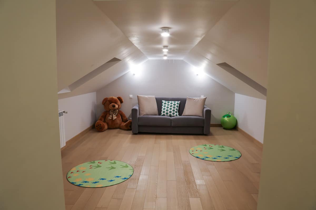Una habitación acogedora en el ático con un sofá gris, un gran oso de peluche y dos alfombras circulares.