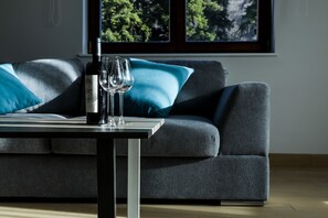 A modern living room with a grey sofa, a small table, and a bottle of wine. - Expecto Apartments (Sinaia)