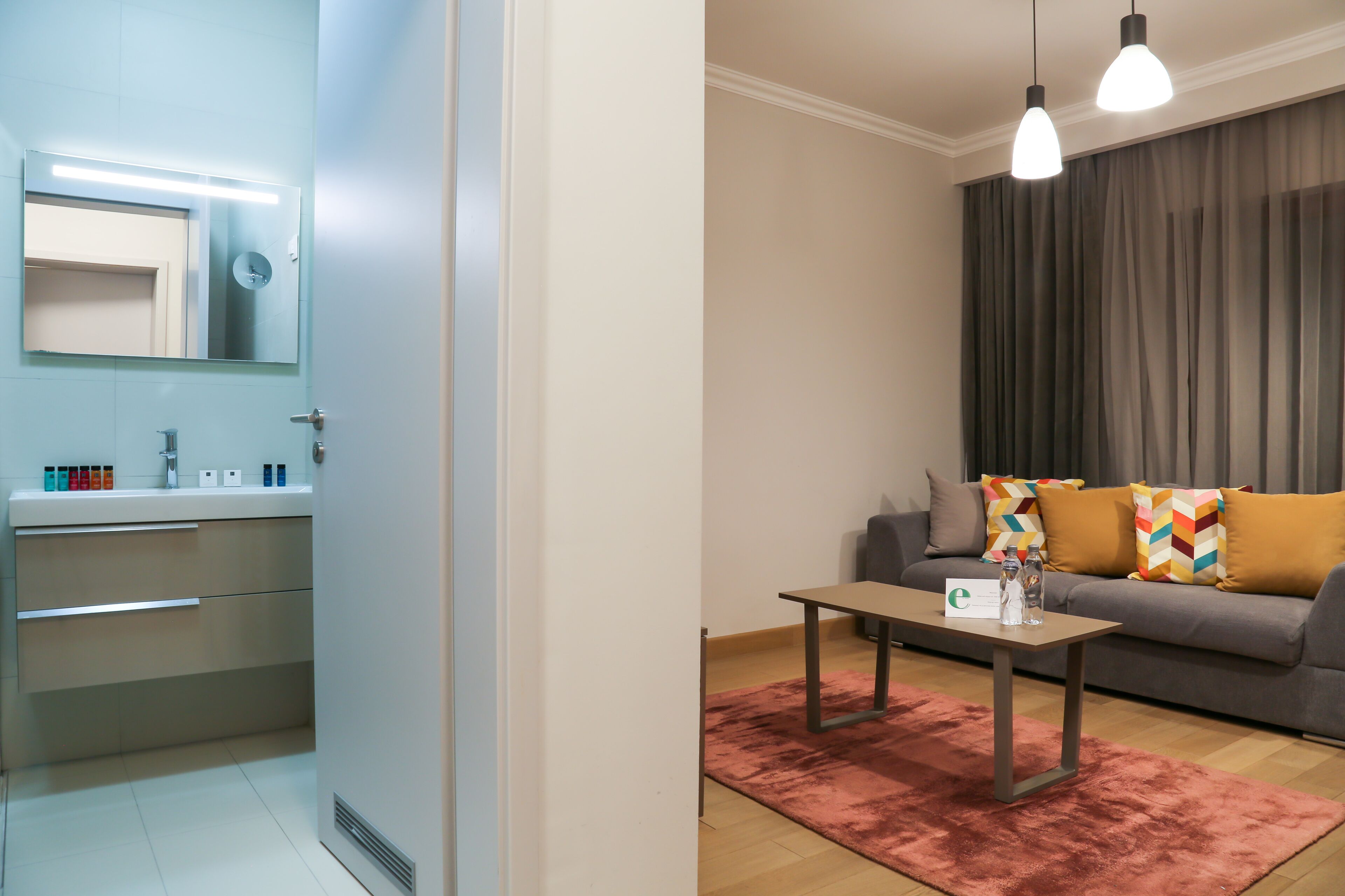 A modern living room with a sofa, a coffee table, and a large window with curtains.