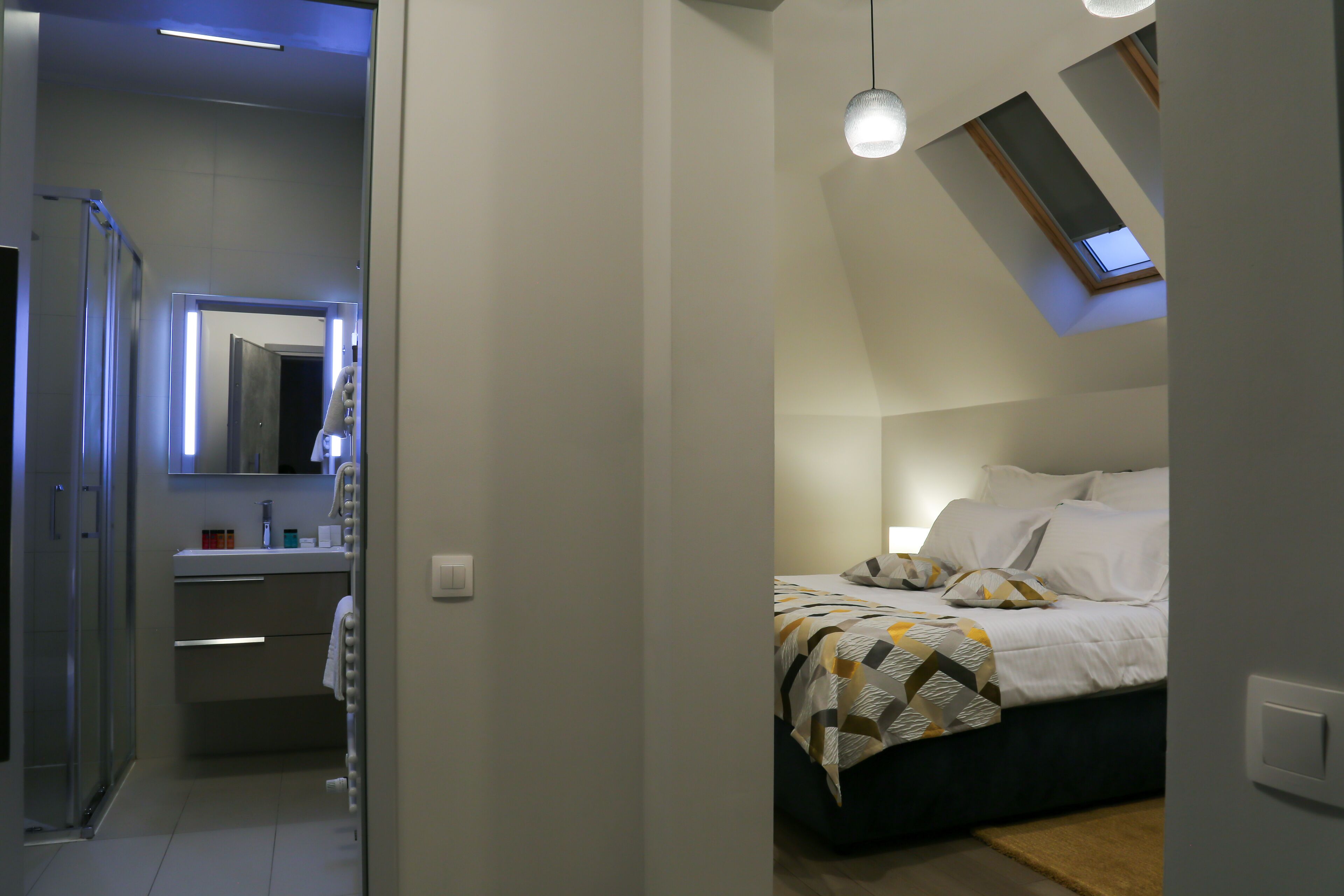A bedroom with a skylight, a bed with patterned bedding, a bedside table, and a nightstand.