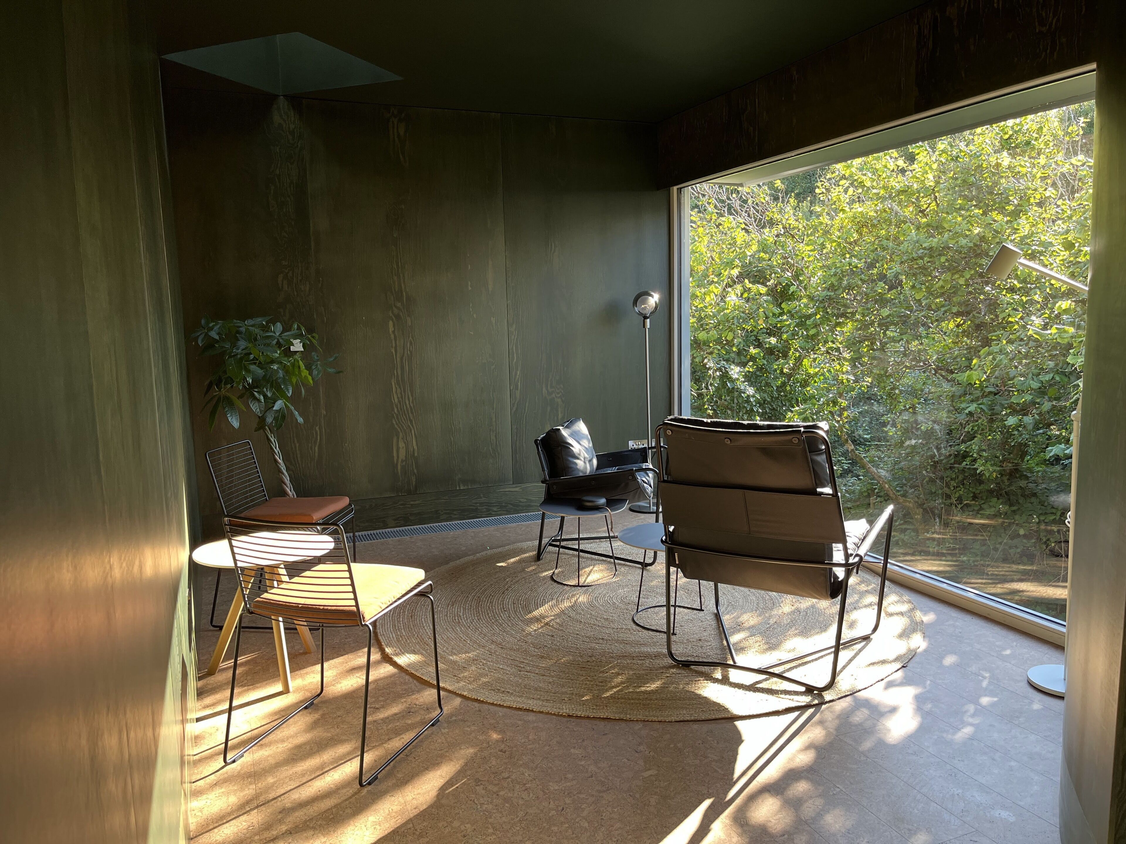 A modern room with a large window, a round table, two chairs, and a floor lamp.