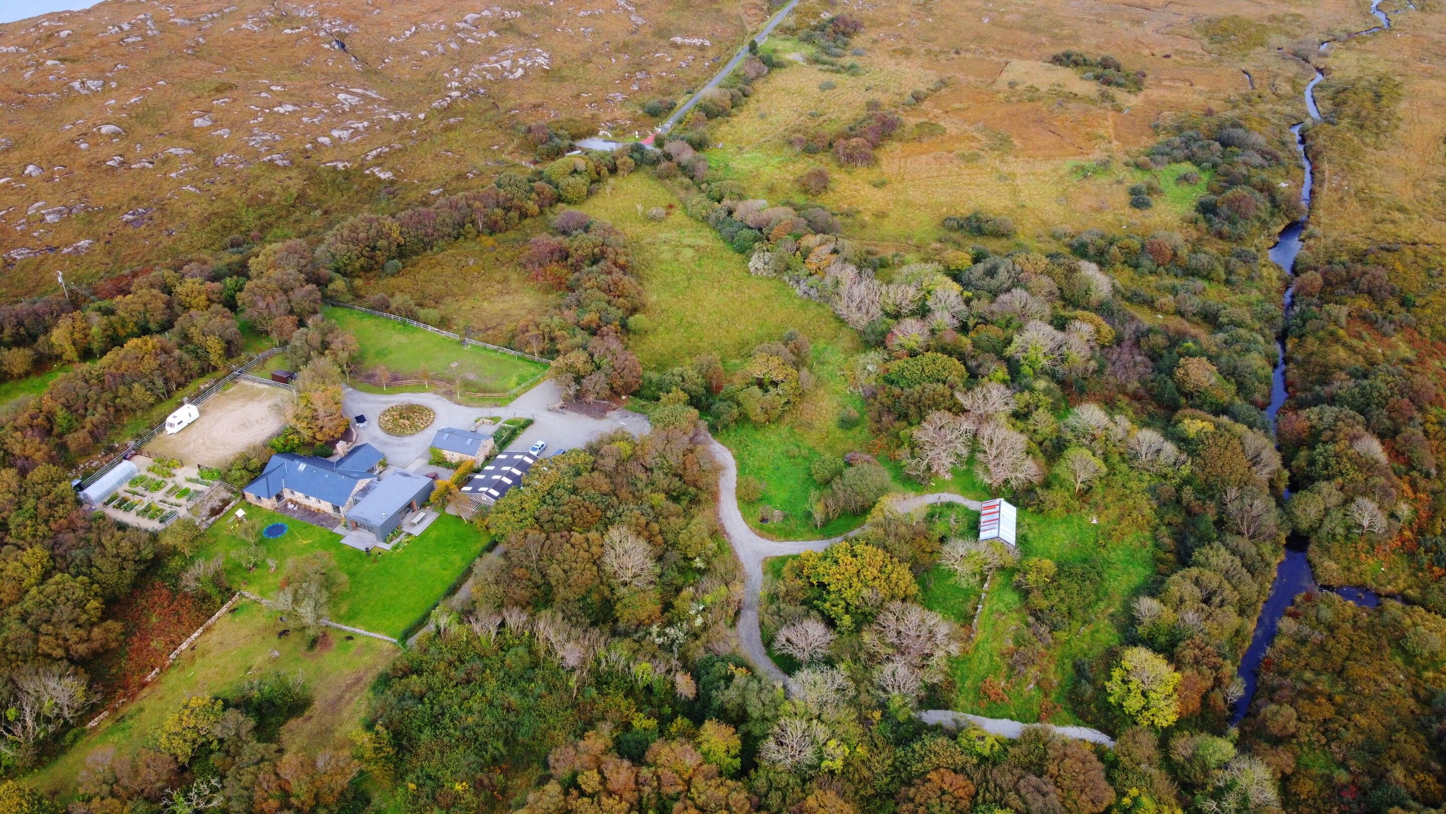 An aerial view of a property with a large open field, a fenced area, and a building with multiple sections.
