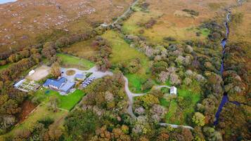 An aerial view of a property with a large open field, a fenced area, and a building with multiple sections.