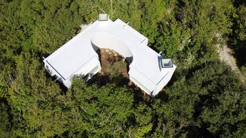 Vista aérea de una casa con una estructura de techo curva distintiva, rodeada de un bosque frondoso.