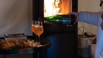 A person pouring a drink into a glass next to a wood-burning stove.
