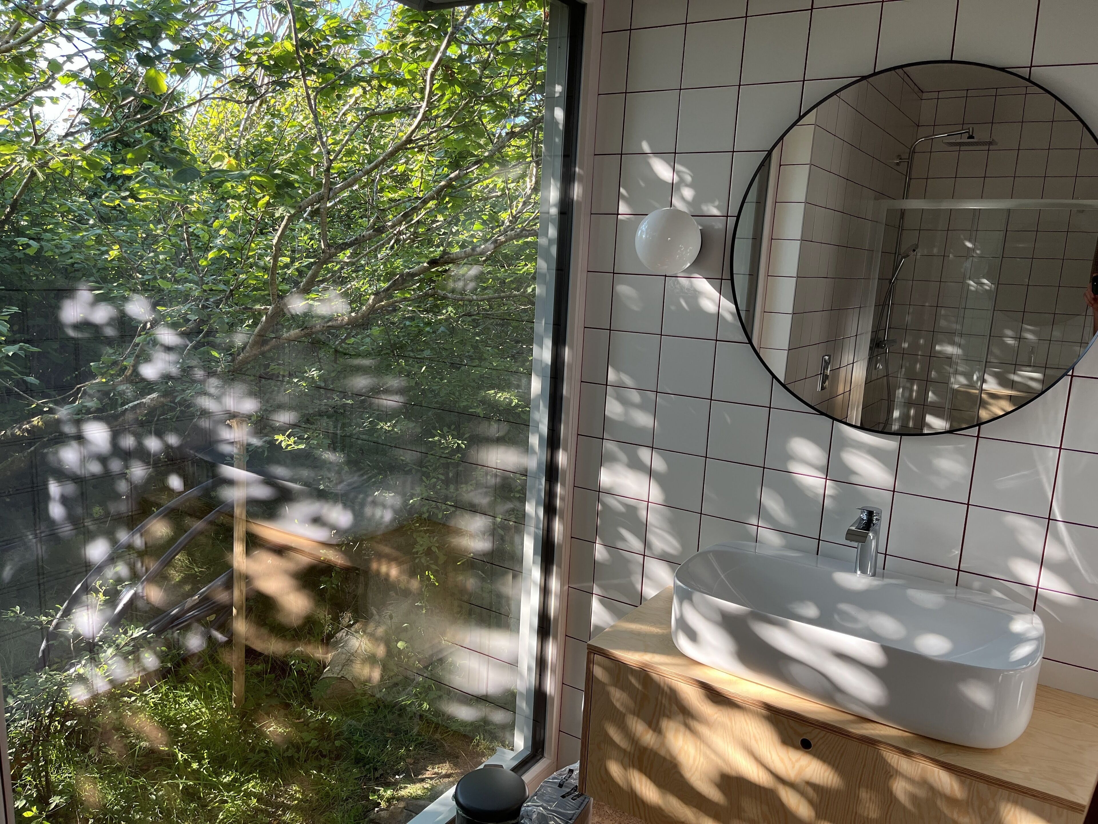 Een badkamer met een groot raam, een ronde spiegel en een witte wastafel.