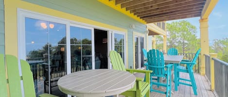 A covered outdoor area with a table and chairs, a sliding glass door, and a wooden deck.