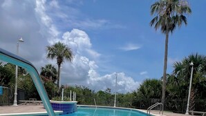 Une piscine d’un bleu éclatant, avec un escalier et des garde-corps en métal, entourée de palmiers et surplombée par un ciel dégagé.