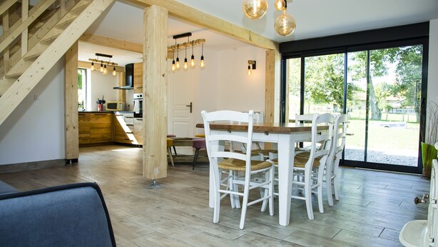 A spacious dining area with a wooden table and white chairs, a staircase leading to an upper level, and a large window offering a view of the outdoors. - Paradis (Cornier)
