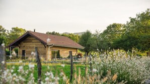 A rustic wooden cabin with a sloped roof, surrounded by a lush garden and a wooden fence. - Paradis (Cornier)