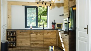 A modern kitchen with wooden cabinetry, a built-in island, a window with a view of greenery, and a stainless steel refrigerator. - Paradis (Cornier)