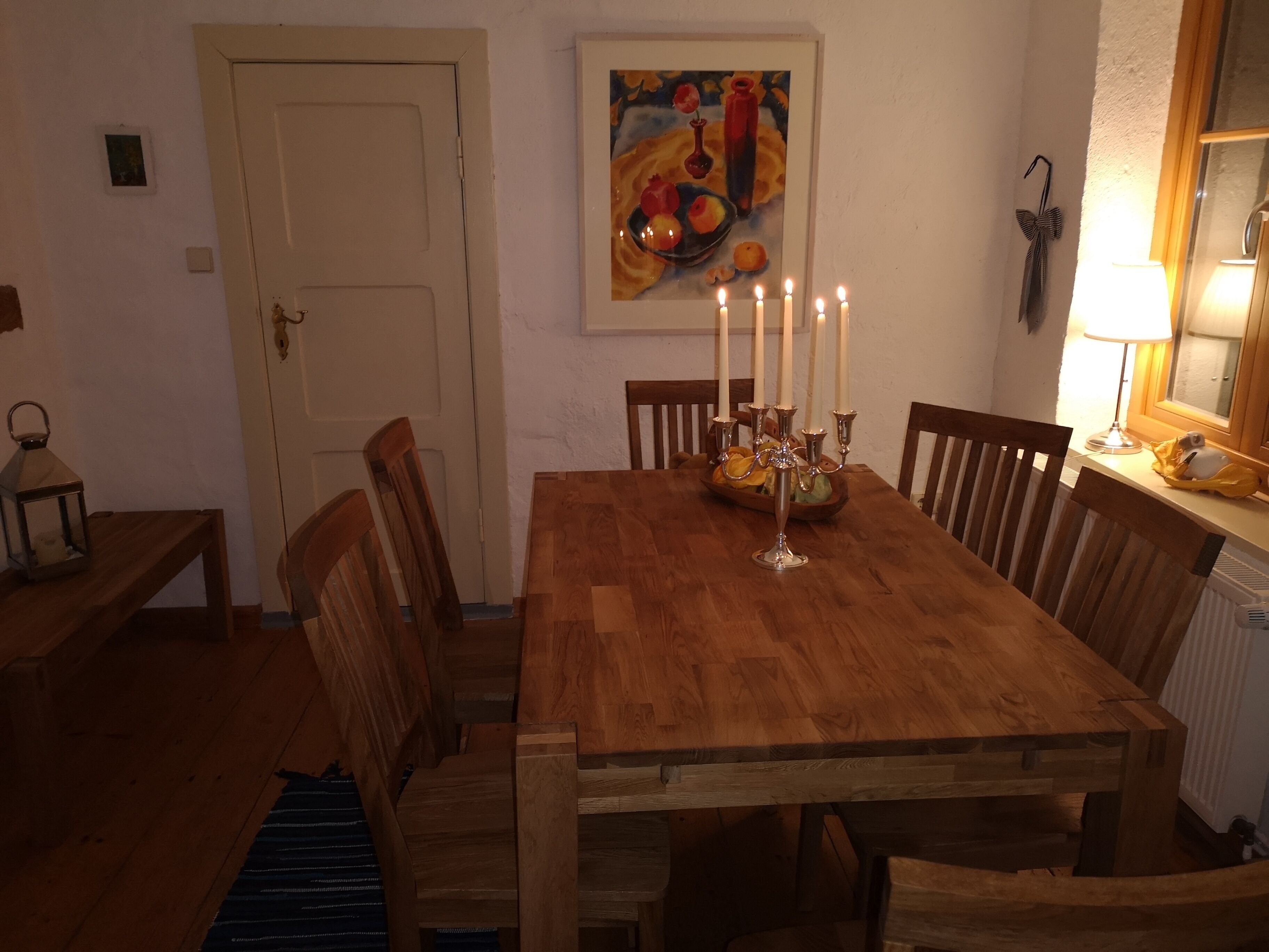 A wooden dining table with six chairs, a candelabra with lit candles, and a painting on the wall.