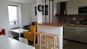 A modern kitchen with a wooden island, a dining area with a white table and yellow chairs, and a brick backsplash. - 100 m from the beach in a pretty family seaside resort (Luc-sur-Mer)