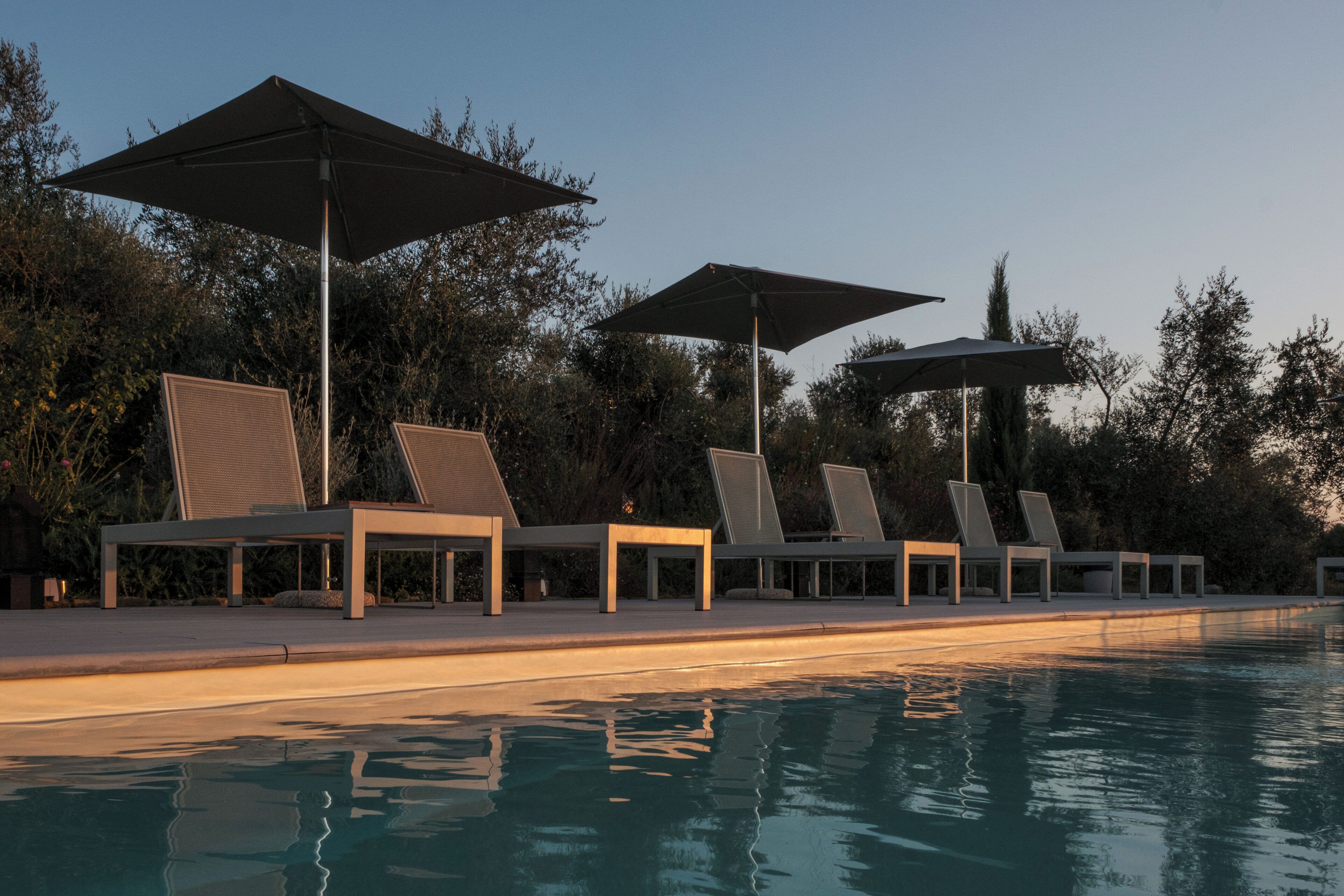 A poolside area with lounge chairs and umbrellas, surrounded by trees.