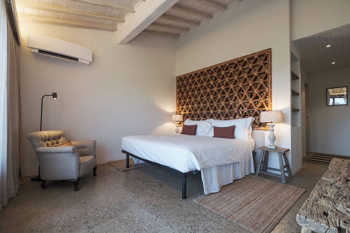 Een slaapkamer met een bed, een stoel, een lamp en een decoratief hoofdeinde.