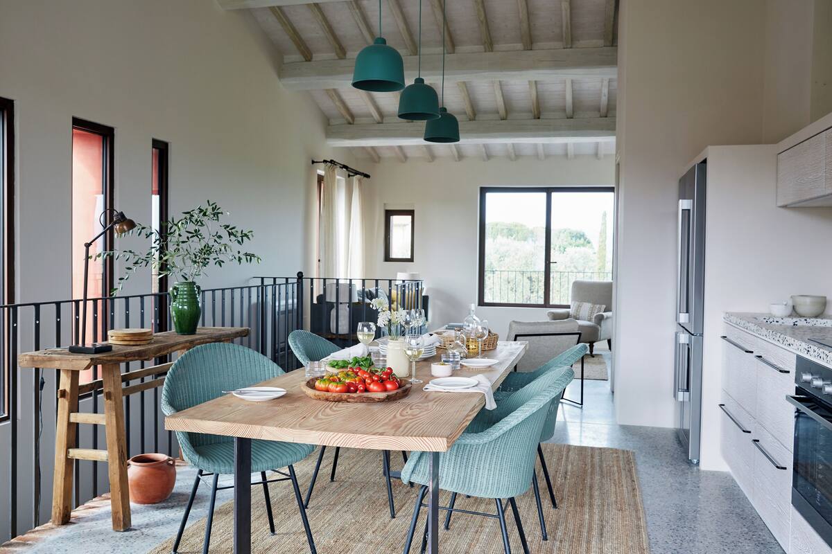 Een eethoek met een houten tafel, teal stoelen en hangende teal hanglampen.