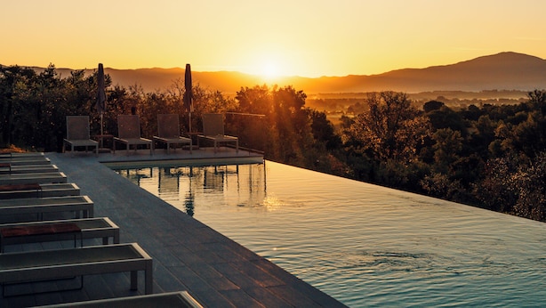 Un espace aménagé au bord de la piscine, avec des chaises longues et une vue sur le coucher de soleil se déclinant sur un paysage vallonné.