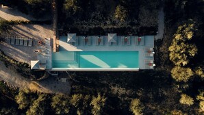 Vista aérea de un moderno resort con una gran piscina, tumbonas y un camino pavimentado.