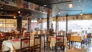 Un restaurante con varias mesas y sillas, piso de baldosas y luces colgantes en el techo.
