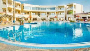 Una piscina de borde curvo, rodeada por un edificio con múltiples balcones y zonas de estar al aire libre.