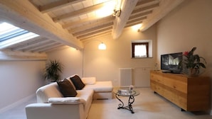 Uma sala de estar moderna com um sofá branco, uma mesa de centro de vidro, um armário de madeira e um radiador.