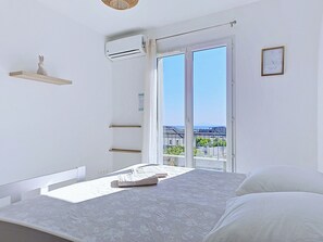 Une chambre avec un lit, une fenêtre donnant sur un paysage agréable, un climatiseur fixé au mur et une petite étagère sur laquelle est posé un objet décoratif.