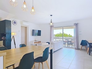 A modern living room with a dining area, a TV mounted on the wall, and a balcony with outdoor furniture.