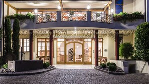 Entrada de un hotel con un balcón de hierro forjado, un cartel que dice "HOTEL SPITALER" y un camino empedrado que conduce a las puertas.