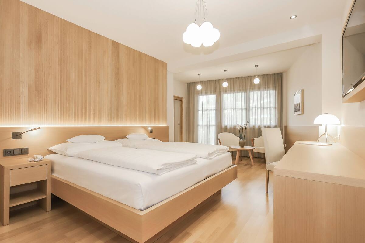A modern hotel room with a large bed, bedside tables, a desk, and a chair.