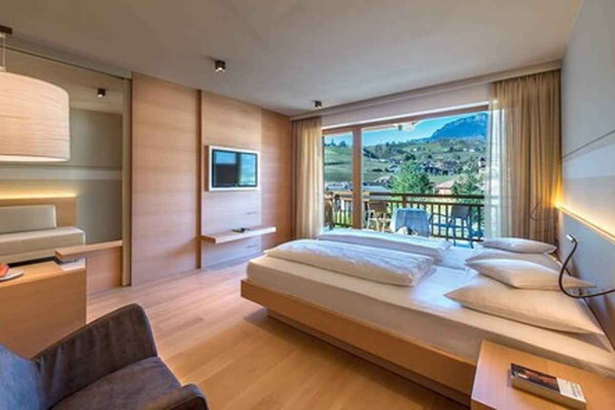 A modern hotel room with a large bed, a TV mounted on the wall, and a balcony with a view of the countryside.
