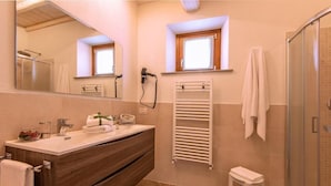 Un baño con tocador de madera, toallero, ducha y ventana.